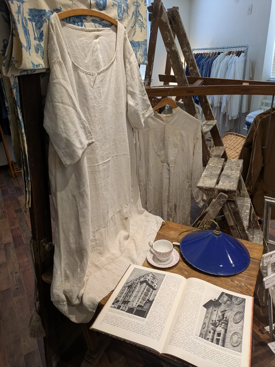 店内のテーブル。リネンのワンピースと古い洋書、琺瑯のランプ