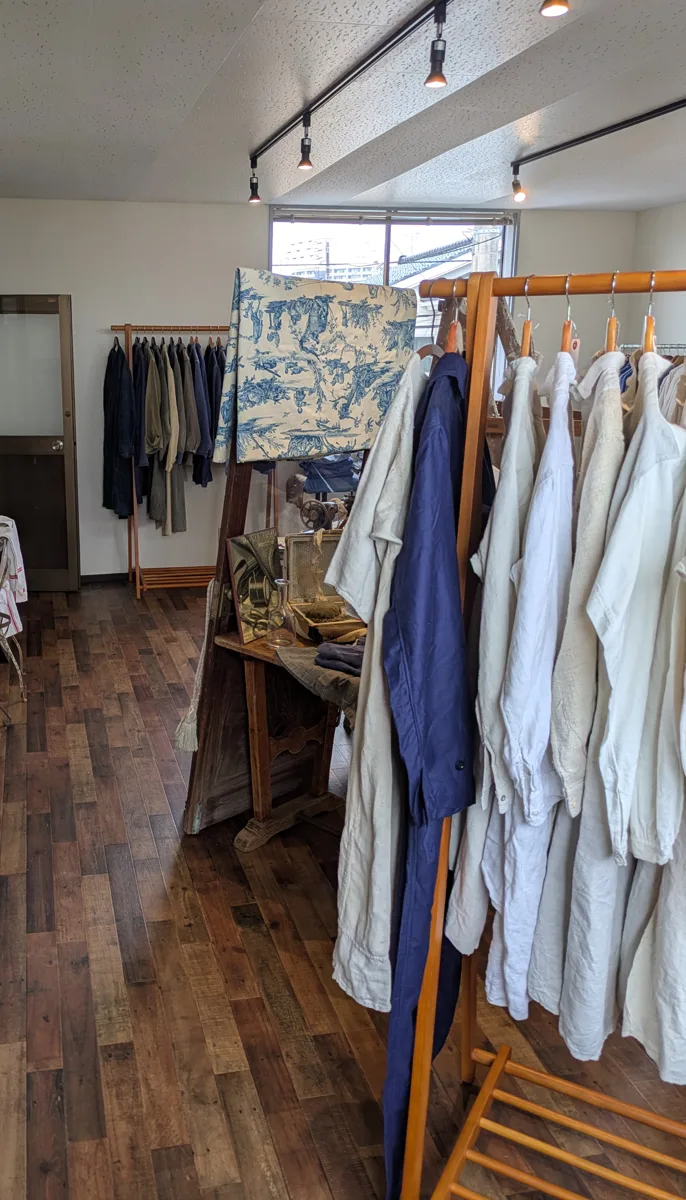 LOGUE店内。窓際のラックに服が並び、木の床の通路と奥のラックが見える。